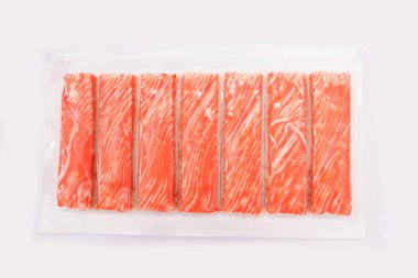 Beyaz arkaplanda paketlenmiş yengeç çubukları.