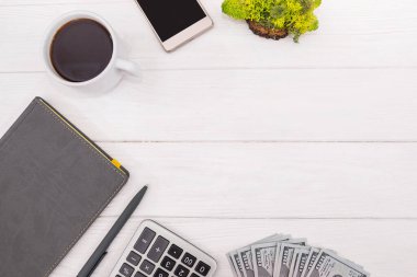 Kalem, akıllı telefon, gözlük, dolar ve ahşap arka planda hesap makinesi olan bir defter. Düz yatıyordu. Yukarıdan bak. Boşluğu kopyala.