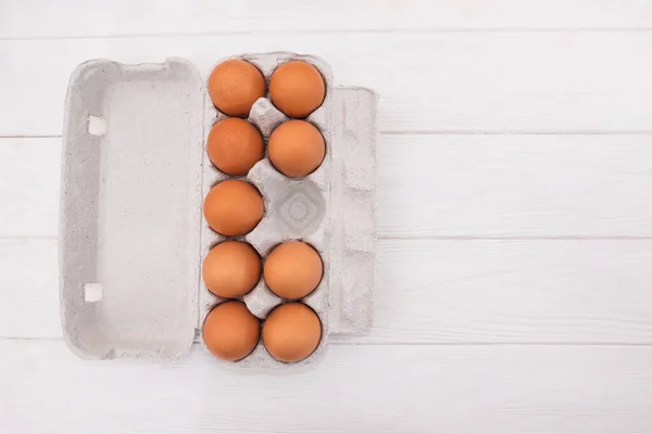 Cardboard tray with chicken eggs without one egg on a wooden background. View from above. Copy space.