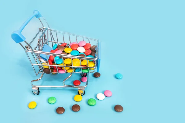 青い背景のショッピングカートの中の丸い色のキャンディー キャンディショッピングのコンセプト 空間のコピー — ストック写真