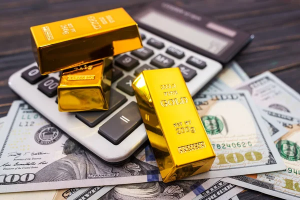 Close-up of gold bars with dollars and a calculator.