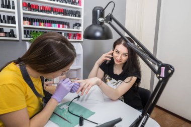 A manicurist covers a client's nails with varnish in a nail salon. Nail care concept.