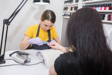 Güzellik endüstrisi konsepti. Eldivenli kadın manikürcü müşteri tırnaklarını törpülüyor. Kozmetik salonunda, klinikte çalışan genç bir kadının portresi. Hijyen ve el bakımı..