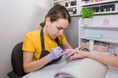 girl master of manicure makes a manicure to a client using a bamboo stick.Beautician's salon, manicure, nail polishing procedure.