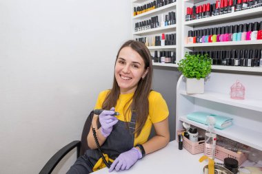 manicurist posing at the camera with a cutter while sitting at a work table in a nail salon.