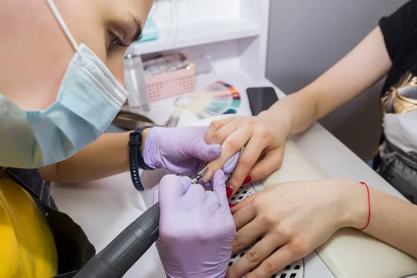 Professional hardware manicure on an electric machine in a beauty salon. The master uses an electric machine to remove nail polish from his hands during a manicure.