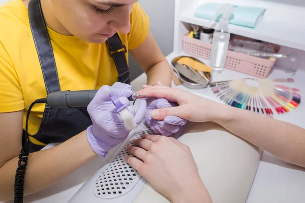 Professional hardware manicure on an electric machine in a beauty salon. The master uses an electric machine to remove nail polish from his hands during a manicure.