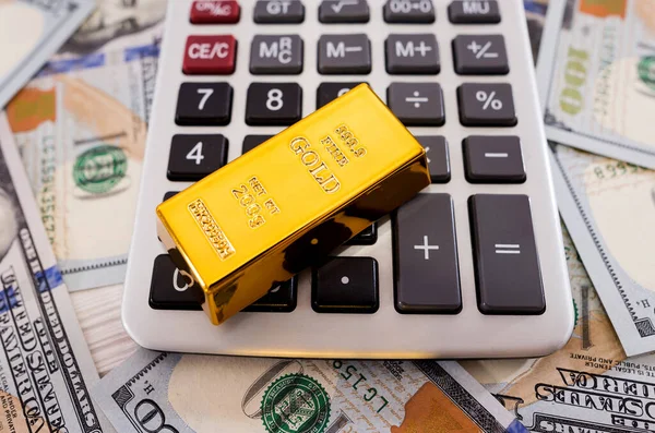 gold bar on a calculator against the background of dollars. Wealth concept.