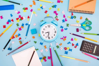Renkli kalemler, çalar saat, not defteri ve mavi arka planda çeşitli okul malzemeleri. Okul konsepti. Okula geri dön..
