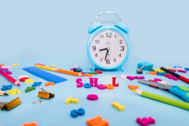 Renkli kalemler çalar saat ve mavi arka planda çeşitli okul malzemeleri. Okul konsepti. Okula geri dön..