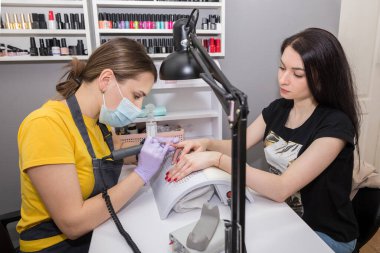 Kadın bir usta kuaförde manikür yaparken elektrikli tırnak makası kullanır. Donanım manikürü yakın plan. El bakımı kavramı.