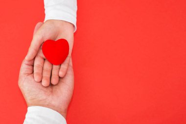 Kırmızı bir arka planda bir anne ve çocuğun ellerinde kırmızı bir kalp. Aşk, merhamet, sempati kavramı