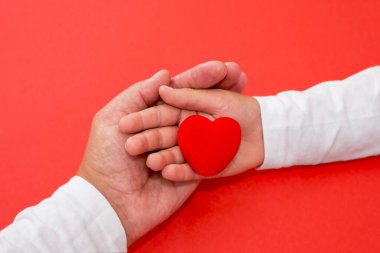 Kırmızı bir arka planda bir anne ve çocuğun ellerinde kırmızı bir kalp. Aşk, merhamet, sempati kavramı
