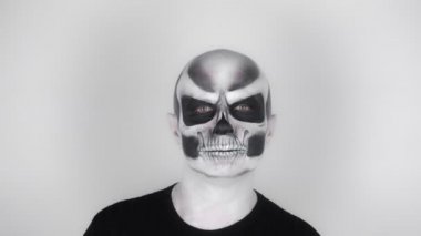 Cadılar Bayramı için iskelet makyajlı neşeli komik adam kameraya gülümseyip dans ediyor. Stüdyoda çekim. Gri arkaplan