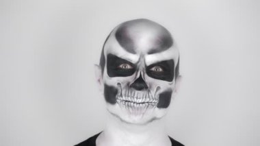 Cadılar Bayramı için iskelet makyajlı neşeli komik adam kameraya gülümser. Stüdyoda çekim. Gri arkaplan