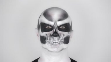 Cadılar Bayramı için iskelet makyajlı neşeli komik adam kameraya gülümser. Stüdyoda çekim. Gri arkaplan