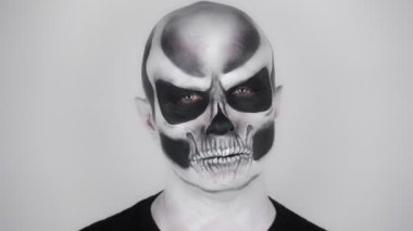 Korkunç bir cadılar bayramı iskeleti makyajlı bir adam kameraya şeytani bir bakışla bakıyor. Stüdyoda çekim. Gri arkaplan