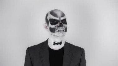 Cadılar Bayramı iskeletindeki takım elbiseli adam kameranın önünde hava atıyor. Stüdyoda çekim. Gri arkaplan