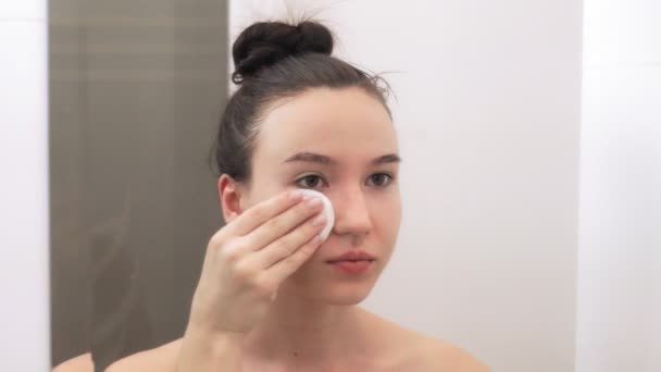 年轻美丽的女孩用棉签擦拭她的脸 这个女孩在镜子中得到了反映 皮肤护理概念 — 图库视频影像
