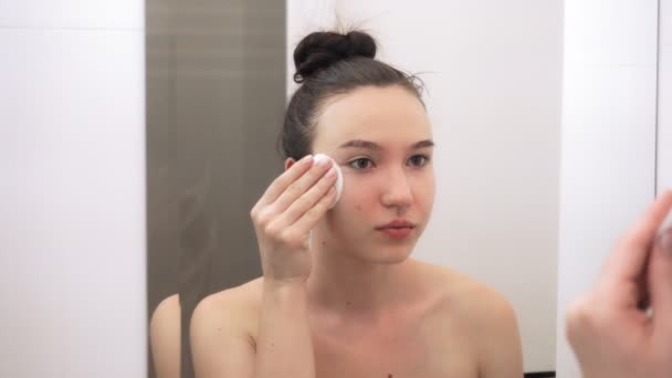 綿棒で彼女の顔をきれいに若い美しい女の子 その少女は鏡に映っている スキンケアコンセプト — ストック動画