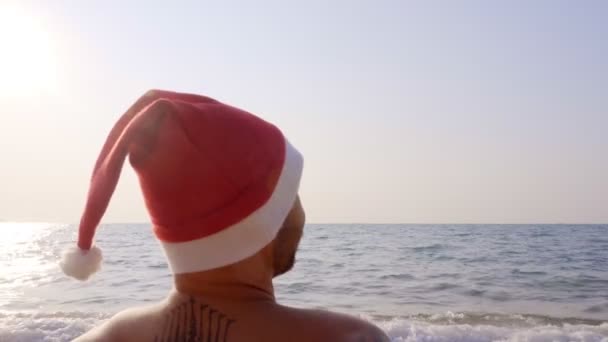 Homem Senta Areia Junto Mar Com Chapéu Pai Natal Feliz — Vídeo de Stock