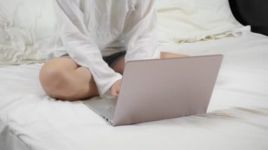 Dizüstü bilgisayarıyla çalışan bir kadın kar beyazı bir yatakta oturuyor.