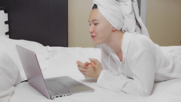 自宅でベッドに座っている間にビデオ通話をするためにラップトップコンピュータを使用して若い女性 — ストック動画
