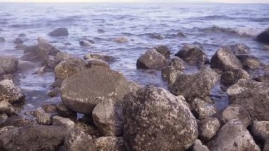 Güneşli bir günde deniz manzarası. Deniz dalgaları taşlara çarpıyor.