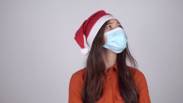 Krásná mladá žena v klobouku Santa Claus v lékařské masce si myslí — Stock video
