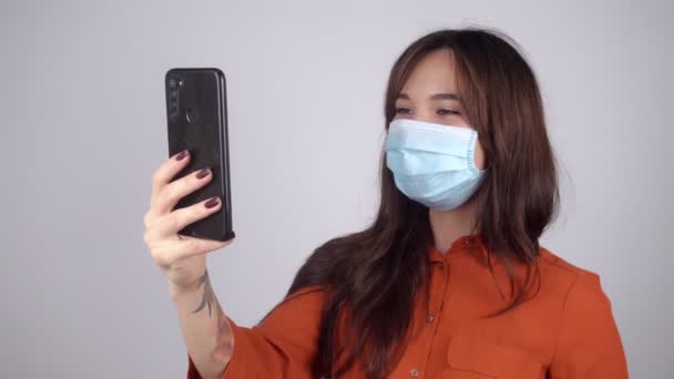 Glückliche junge Frau in medizinischer Maske mit Telefon in der Hand kommuniziert per Videoanruf — Stockvideo