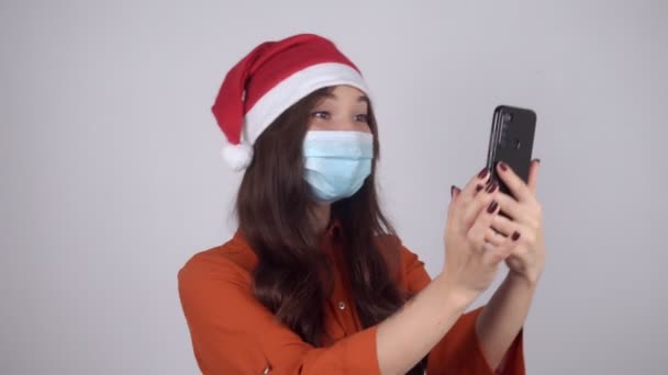 산타 모자를 쓴 채로 의료용 마스크를 쓰고 전화 통화를 하는 여성 — 비디오