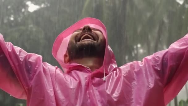 身穿粉色雨衣的快乐大胡子男人在热带雨中湿透了 然后举起双手 高质量的4K镜头 — 图库视频影像