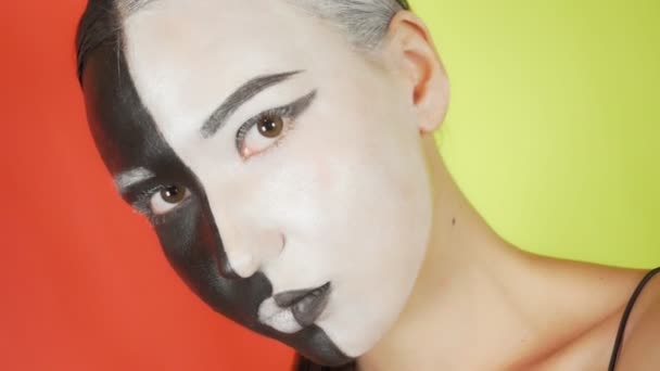 Una Joven Con Maquillaje Blanco Negro Mira Cámara Fondo Color — Vídeos de Stock