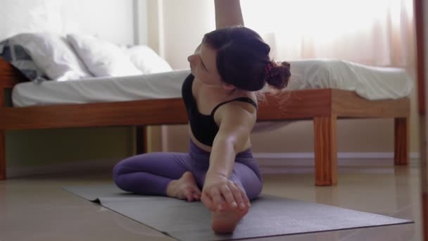 Jovem mulher senta-se em um tapete esportivo e realiza um exercício de ginástica — Vídeo de Stock