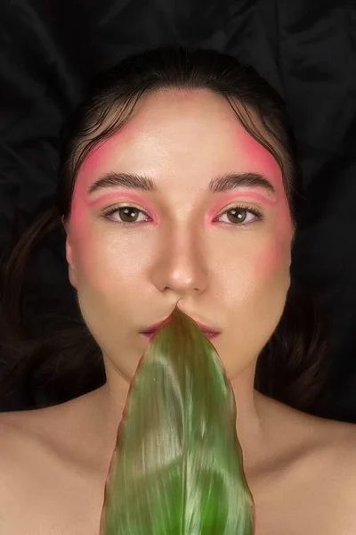 Parlak makyajlı, yeşil bir tropikal yaprak tutan modaya uygun bir model..
