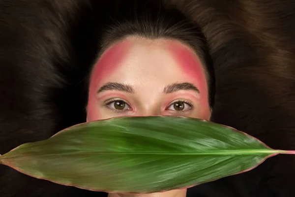 Parlak makyajlı, yeşil bir tropikal yaprak tutan modaya uygun bir model..