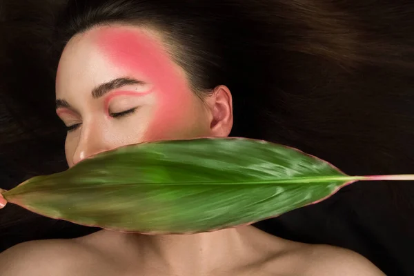 Parlak makyajlı, yeşil bir tropikal yaprak tutan modaya uygun bir model..