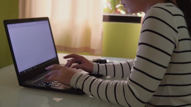 En frilans kvinna sitter vid ett skrivbord och arbetar på en bärbar dator. — Stockvideo
