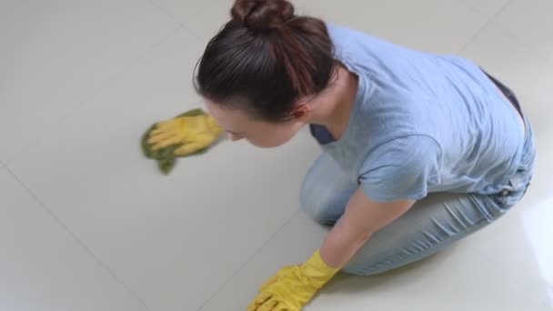 Mujer joven con guantes amarillos lava el suelo. Mujer limpia la suciedad en baldosas blancas — Vídeo de stock