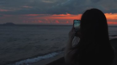 Bir kadın cep telefonuyla gün batımını fotoğraflıyor.. 