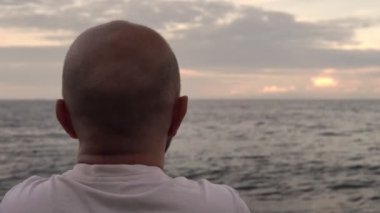 Deniz kıyısında oturan bir adam güzel gökyüzüne hayran.
