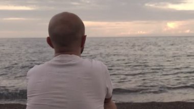 Deniz kıyısında oturan bir adam güzel gökyüzüne hayran.