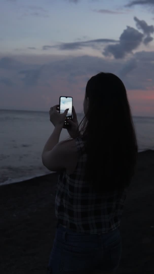 Une femme photographie le coucher du soleil avec son téléphone portable. Tournage vertical — Video