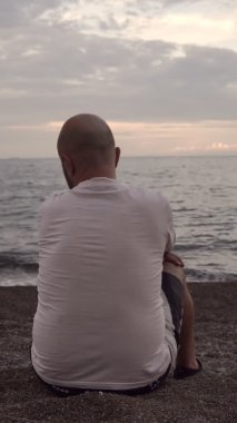 Deniz kıyısında oturan bir adam güzel gökyüzüne hayran olur. Dikey çekim