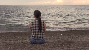 Genç bayan sahilde oturuyor ve deniz manzarasının tadını çıkarıyor.