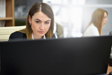 Modern bir ofiste masaüstü bilgisayarında çalışan konsantre orta yaşlı bir kadın.