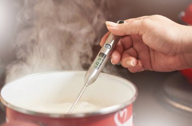 Kadın eli, tavadaki sıcaklığı elektronik pişirme termometresiyle ölçer.