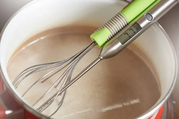 Cozinha que mede o termômetro de cozinha e bata em uma panela com creme quente — Fotografia de Stock