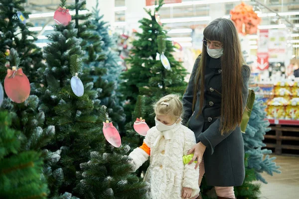 Мама з дочкою в масках вибирають христмас в магазині. — стокове фото