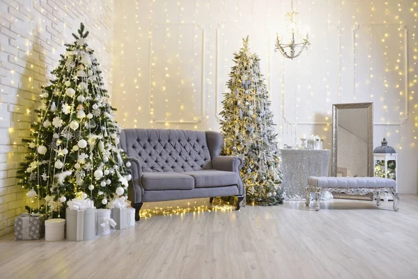 Oturma odasında Noel süsleri, gri bir kanepe, duvarında iki Noel ağacı ve çelenk.